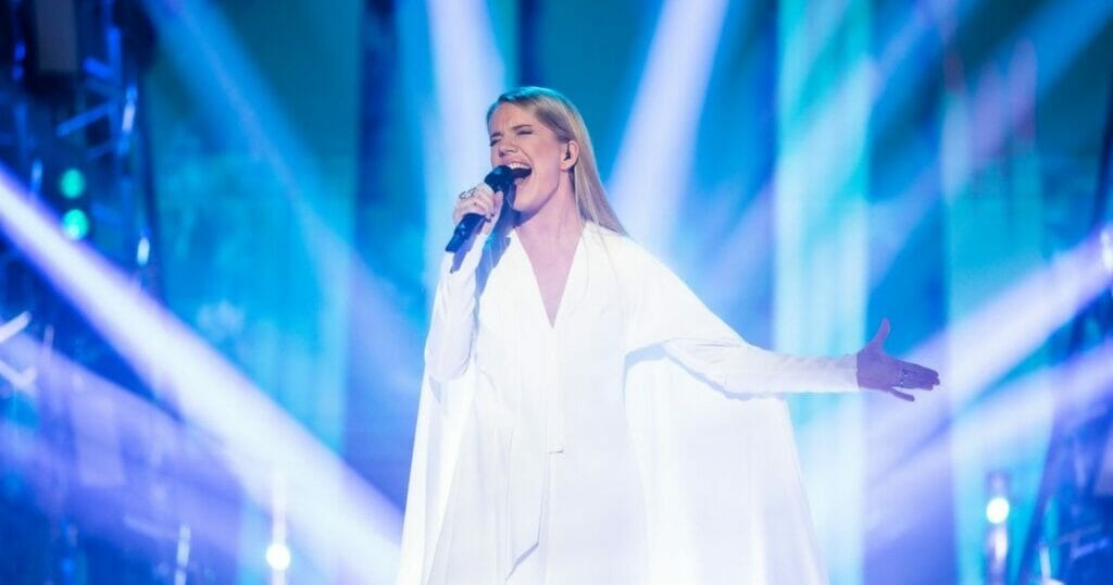 A woman in a white dress serenading into a microphone.