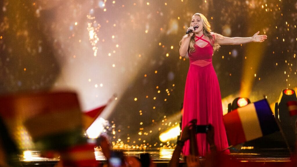 A woman in a red dress singing in front of a crowd of flags during a patriotic event.