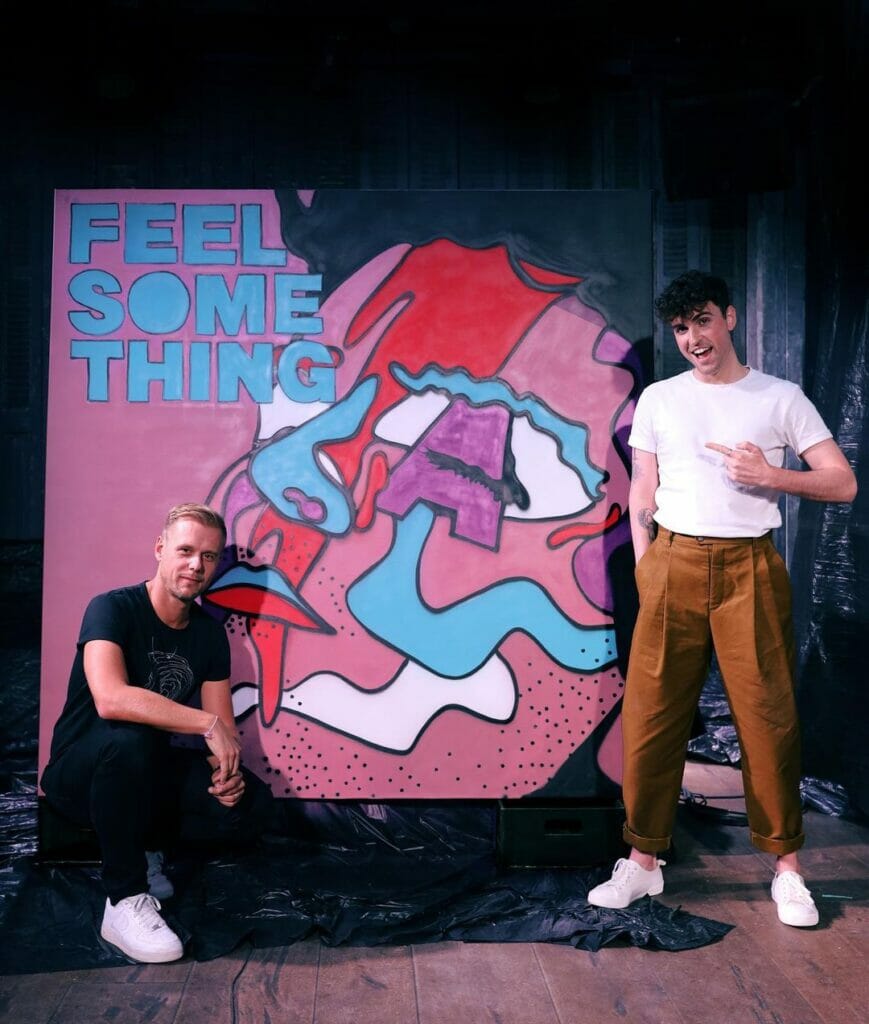 Two men standing in front of a painting with the words feel something thing, pondering its meaning and significance.