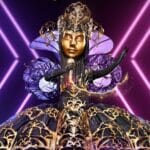 An image of a woman in a purple dress holding a microphone.