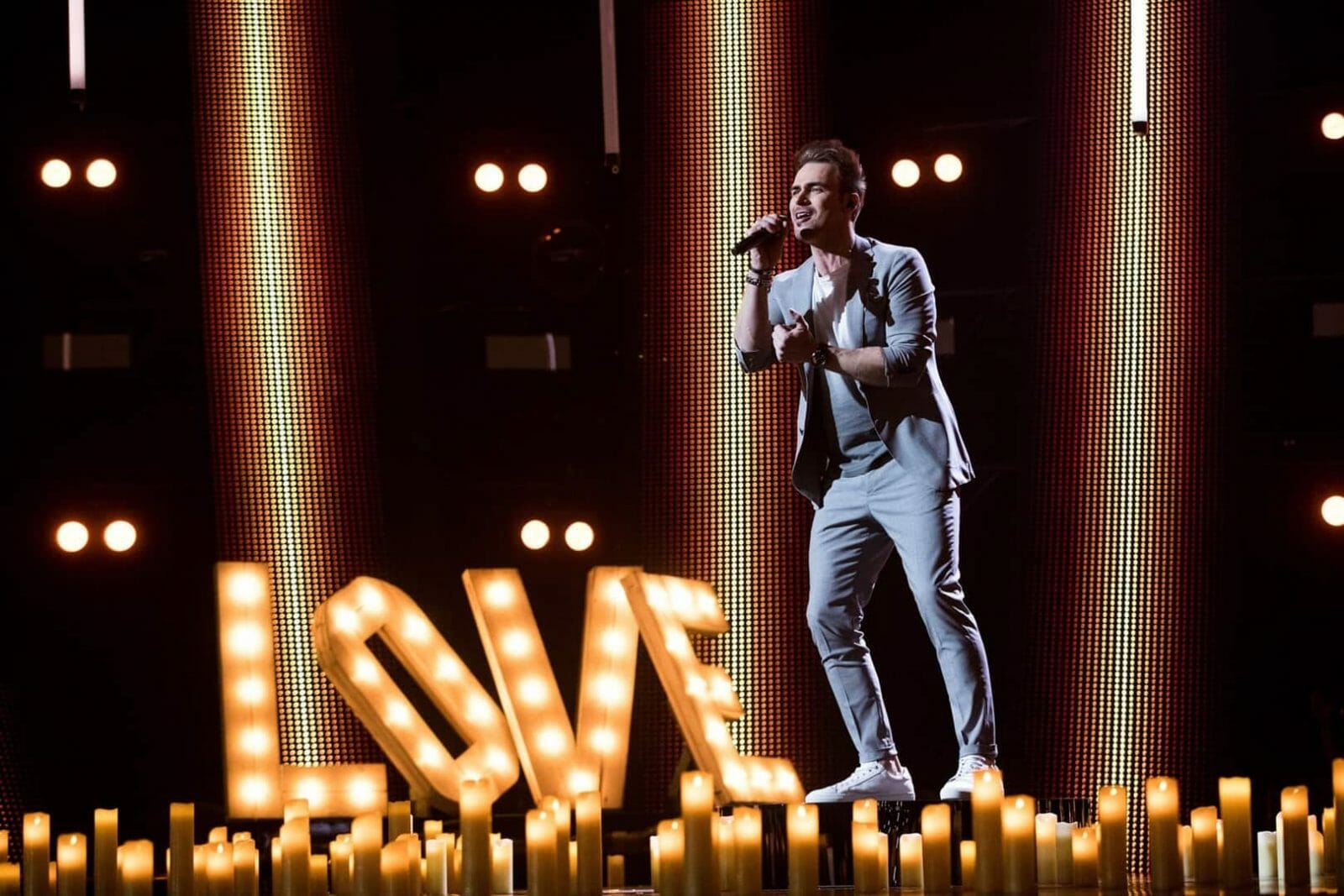 A man in a suit standing in front of candles, creating a romantic ambiance.